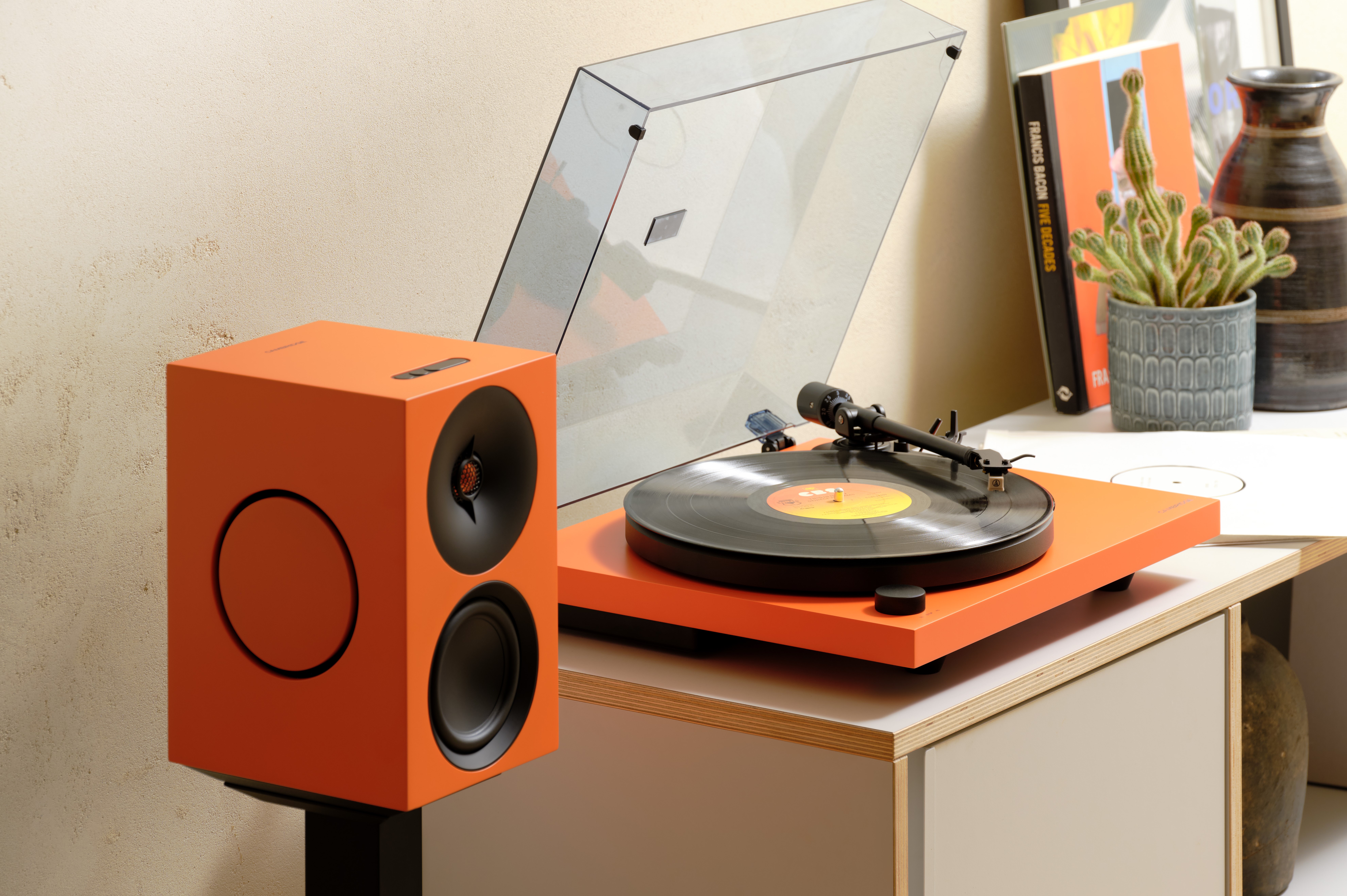 Cambridge audio Spira platespiller med L/R X aktive høyttalere sammen i en hifi pakke. Lifestyle bilde i fargen oransje i en stue